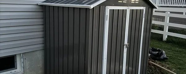 Metal storage shed assembled beside a house